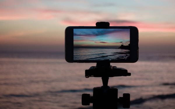 Ein Smartphone klemmt auf einem Stativ, um den Sonnenuntergang einzufangen.