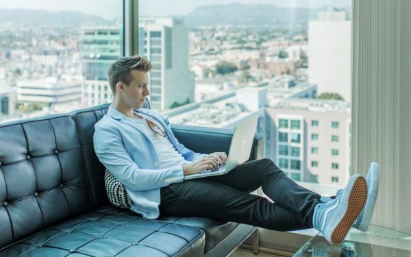 Ein junger Mann sitzt auf dem Sofa und surft am Laptop.