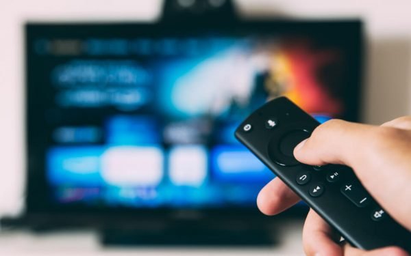 Eine Fernbedienung deutet auf ein TV-Gerät. Der Zuschauer nutzt Internetfernsehen.