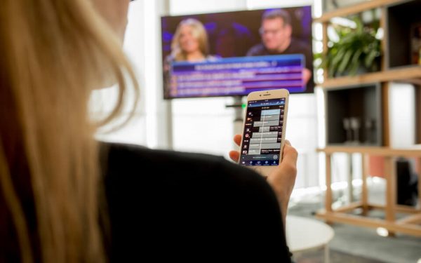 Eine TV-Zuschauerin sieht eine Quizsendung. Über das Smartphone Smartphone rätselt sie mit. IPTV macht solche Interaktion möglich.