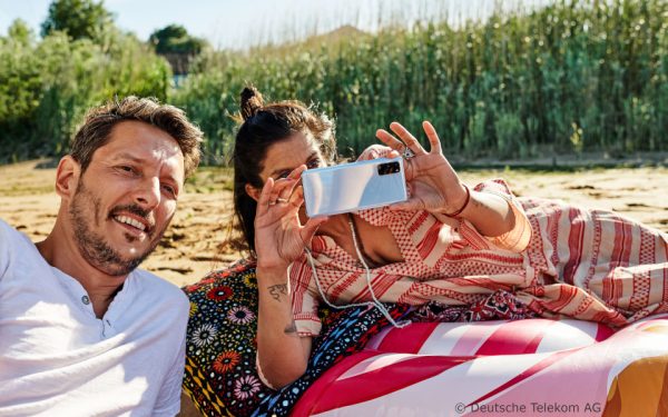 Ein Paar entspannt beim Picknick. Die Frau fotografiert mit ihrem Smartphone.