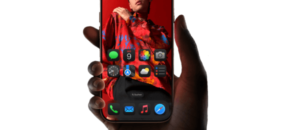 Hand hält ein iPhone 16 Pro Max, auf dessen Display ein Mann in roter Kleidung vor rotem Hintergrund zu sehen ist, darunter App-Symbole des Startbildschirms.