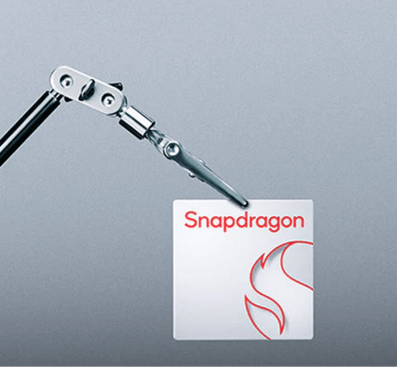 Mechanischer Greifarm hlt ein Snapdragon-Prozessor-Plttchen mit rotem Logo auf grauem Hintergrund.