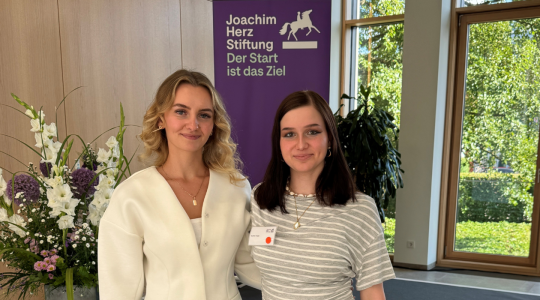 Zwei Personen bei einer Veranstaltung der Joachim Herz Stiftung vor einem Stiftungsbanner in einem hellen Veranstaltungsraum.